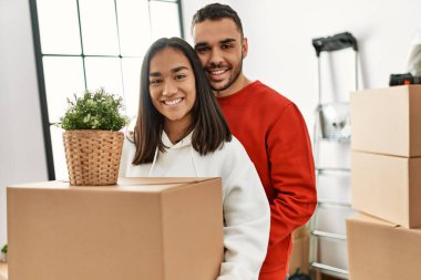 Genç Latin çift mutlu bir şekilde gülümsüyor. Yeni evlerinde karton kutu tutuyorlar..