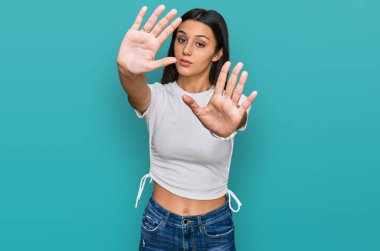 Latin asıllı genç bir kız, günlük beyaz tişört giyiyor, el ve parmaklarıyla çerçeve yapıyor, kamera bakış açısı var. 