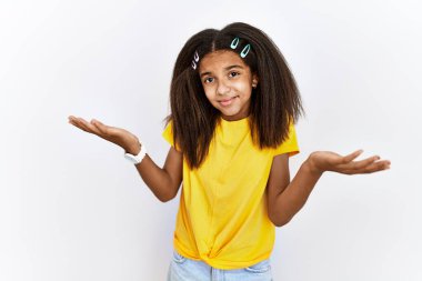 Young african american girl standing over white isolated background clueless and confused expression with arms and hands raised. doubt concept. 