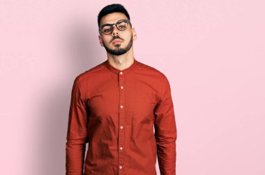 Sakallı, iş gömleği ve gözlüklü, yüzünde ciddi bir ifadeyle rahatlamış genç bir İspanyol. Basit ve doğal bir şekilde kameraya bakıyorsun.. 