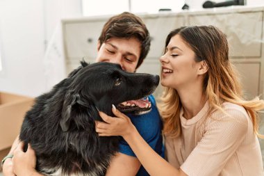 Genç beyaz çift mutlu bir şekilde gülümsüyor. Yeni evlerinde yerde köpekleriyle oturuyorlar..