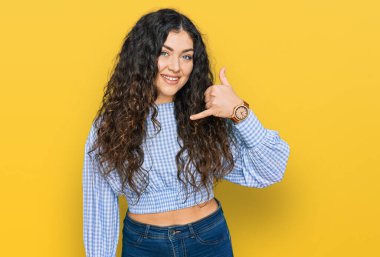 Günlük kıyafetler giymiş, gülümseyen, el ve parmaklarıyla telefon hareketi yapan, telefonda konuşur gibi genç İspanyol bir kız. iletişim kavramları. 