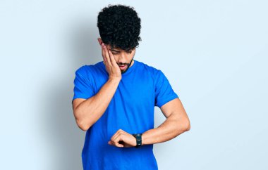 Sakallı, sıradan mavi tişörtlü genç bir Arap. Saate bakıyor. Endişeli, geç kalmaktan korkuyor. 