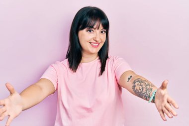 Gündelik giysiler giymiş genç İspanyol kadın kameraya bakıp sarılmak için kollarını açmış gülümsüyor. Mutluluğu kucaklayan neşeli bir ifade.. 