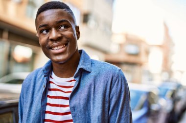 Genç Afrikalı Amerikalı adam gülümseyerek şehirde mutlu mesut duruyor..