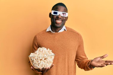 Genç Afro-Amerikalı adam elinde patlamış mısırla zaferi kutluyor mutlu bir gülümsemeyle ve elini kaldırmış bir ifadeyle. 