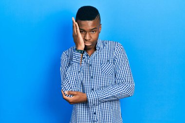 Genç, Afro-Amerikalı bir adam günlük kıyafetler giyip kollarını kavuşturup depresyondan sıkılmış ve yorgun görünüyor.. 