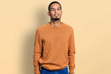 Gündelik kıyafetler giyen genç Afro-Amerikan adam yüzünde ciddi bir ifadeyle rahatlamış. Basit ve doğal bir şekilde kameraya bakıyorsun.. 