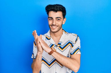 Latin asıllı genç adam, günlük kıyafetler giyip alkışlıyor ve mutlu, neşeli ve gururlu elleri bir arada alkışlıyor. 