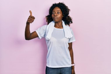 Genç Afrikalı Amerikalı kadın spor kıyafetleri ve havlu giyiyor gururlu görünüyor, gülümsüyor yan tarafa başparmak hareketi yapıyor. 