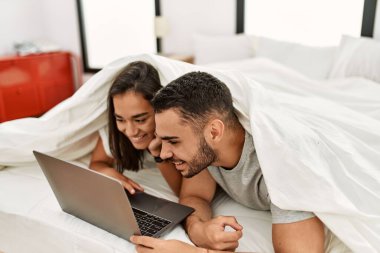 Yatağın üzerinde çarşafla film izleyen genç latin çift..