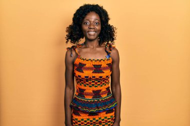 Geleneksel Afro-Amerikan kıyafetleri giyen, yüzünde mutlu ve havalı bir gülümseme olan genç bir Afro-Amerikan kadını. şanslı kişi. 