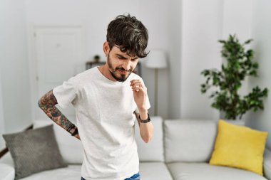 Evdeki oturma odasında sakallı İspanyol bir adam sırt ağrısı çekiyor, elleriyle dokunuyor, kas ağrısı çekiyor. 