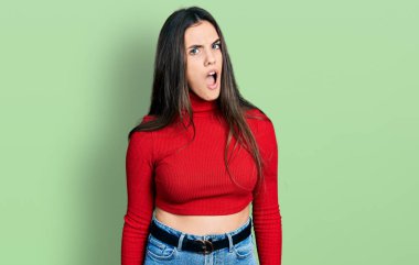 Şok suratlı, kırmızı balıkçı yaka kazak giyen genç esmer, şüpheci ve alaycı görünüyor, ağzı açık kalınca şaşırıyor. 