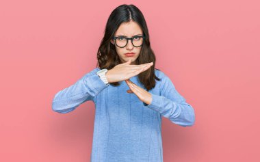 Gündelik kıyafetler ve gözlük takan genç ve güzel bir kadın. Elleriyle jest yapıyor. Hayal kırıklığına uğramış ve ciddi bir yüz ifadesi var. 