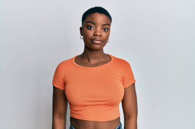 Sıradan turuncu tişört giyen genç Afro-Amerikan kadın yüzünde ciddi bir ifadeyle rahatladı. Basit ve doğal bir şekilde kameraya bakıyorsun.. 