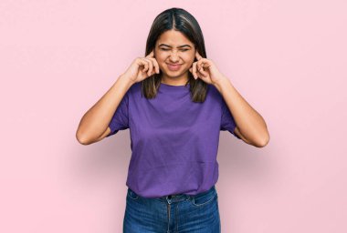 Gürültülü müzik sesi için günlük mor t-shirt giyen genç İspanyol kız kulaklarını parmaklarıyla kapatıyor. sağır kavramı. 
