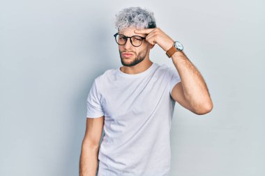 Modern boyalı saçlı, beyaz tişörtlü ve gözlüklü, alnındaki sivilceden mutsuz olduğunu gösteren Latin kökenli genç bir adam. Siyah başlıklı çirkin bir enfeksiyon. sivilce ve deri problemi 