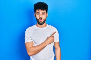 Sakallı, sıradan beyaz tişörtlü genç bir Arap parmağını yana uzatmış, ağzı açık, şaşkın bir ifade sergiliyor.. 