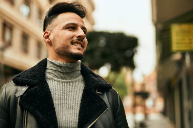 Genç Arap adam gülümsüyor, mutlu bir şekilde şehirde duruyor..