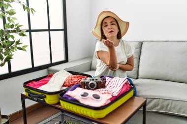 Güzel, orta yaşlı, İspanyol bir kadın valizine yazlık giysiler koyup kameraya bakıyor ve havada bir öpücük savuruyor. Güzel ve seksi. aşk ifadesi. 