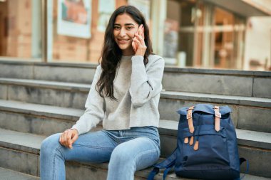 Genç ortadoğulu kız gülümsüyor. Şehirdeki akıllı telefondan konuşuyor..
