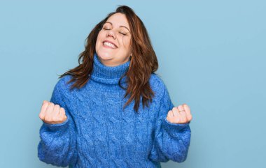 Genç ve cüsseli bir kadın gündelik kıyafetler giyiyor. Çok mutlu ve heyecanlı. Kolları havada, gülümseyen ve başarı için çığlık atan kazanan bir jest yapıyor. kutlama konsepti. 