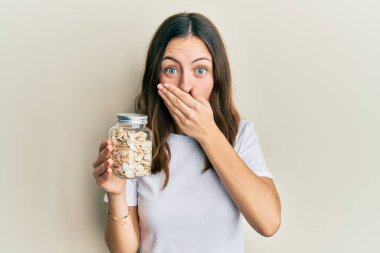 Genç esmer kadın elinde balkabağı çekirdekleri tutuyordu. Ağzı eliyle kaplıyordu. Şok olmuştu ve hata yapmaktan korkuyordu. şaşırmış ifade 