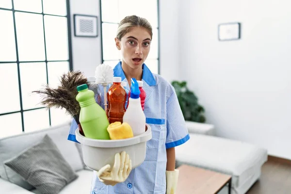 身穿干净制服的金发年轻女子拿着清洁用品 满嘴惊讶地惊愕不已 满脸诧异 — 图库照片