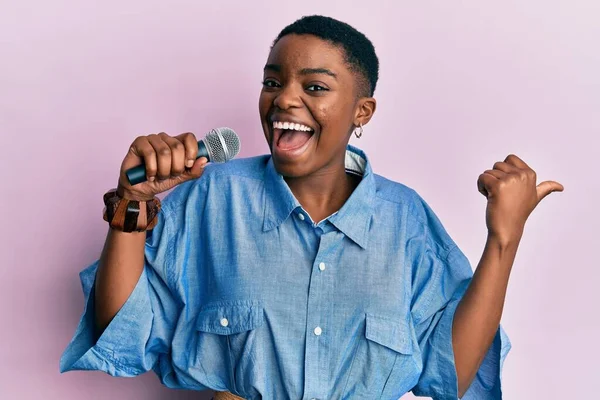 Joven Mujer Afroamericana Cantando Canción Usando Micrófono Apuntando Pulgar Hacia —  Fotos de Stock