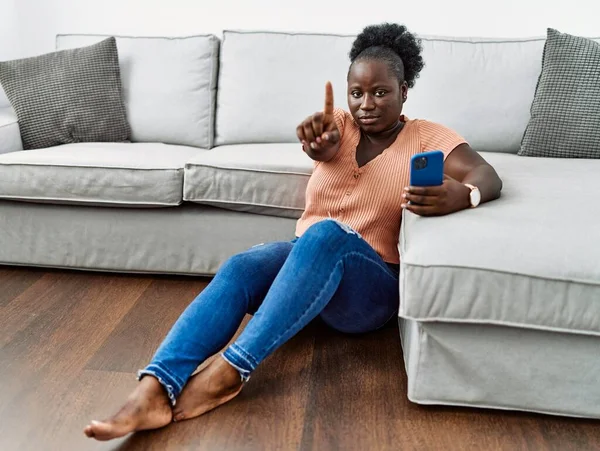 Jovem Africana Usando Smartphone Sentado Chão Casa Apontando Com Dedo — Fotografia de Stock