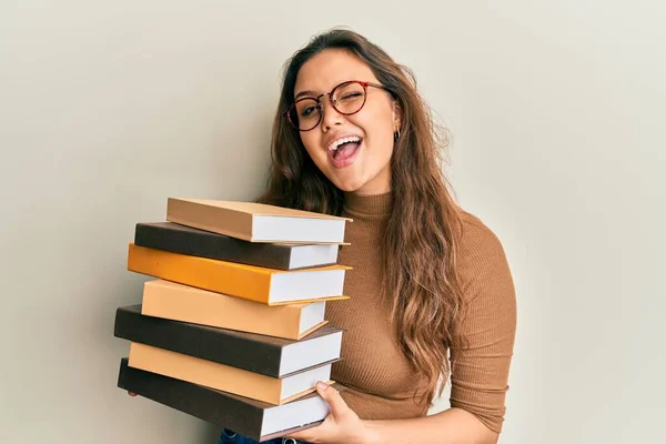 Joven Chica Hispana Sosteniendo Montón Libros Guiñando Ojo Mirando Cámara — Foto de Stock