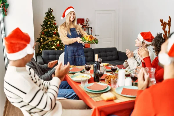 一群人聚在一起鼓掌 坐在桌子上 妇女站在那里举着烤火鸡在家里庆祝圣诞节 — 图库照片