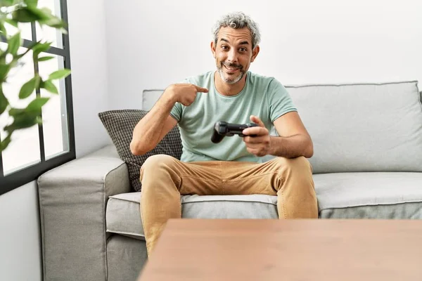 中年时 他的惊慌失措的男人坐在沙发上玩电子游戏 指指点点着一个快乐而自豪的自我微笑 — 图库照片