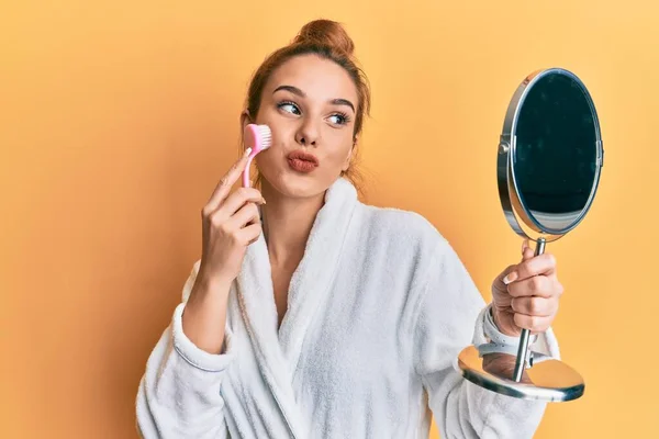 Joven Mujer Rubia Vistiendo Bata Sosteniendo Cepillo Removedor Maquillaje Mirando — Foto de Stock
