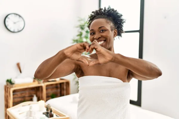 美しさの中心に立ってタオルを身に着けている若いアフリカ系アメリカ人女性は 手でハートのシンボルと形状を示す愛に微笑む ロマンチックなコンセプト — ストック写真