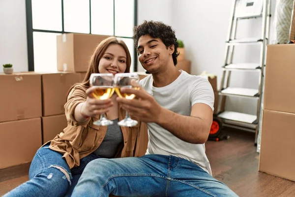 Genç çift yeni evinde kadeh kaldırırken mutlu bir şekilde gülümsüyor..
