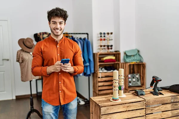 若いヒスパニック店主の男が服屋で働くスマートフォンを使って笑顔で幸せ — ストック写真