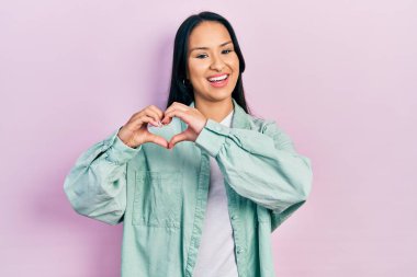 Güzel İspanyol bir kadın, burun piercingli, sıradan yeşil bir ceket giyiyor, aşıkken gülümsüyor, elleriyle kalp sembolü yapıyor. romantik kavram. 