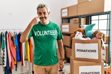 Bağışta gönüllü tişört giyen orta yaşlı İspanyol bir adam el ve yüz yüze, gülümseyen bir gülümsemeyle ayakta duruyor. güzellik konsepti 