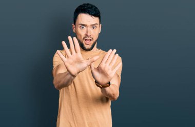 Sakallı, sıradan tişörtlü, korku ifadesinden korkmuş ve dehşete düşmüş İspanyol bir adam. El kol hareketi yapmayı kes, şok içinde bağır. panik konsepti. 