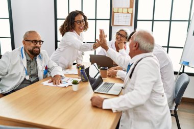 Klinikte el ele tutuşup gülümseyen orta yaşlı bir doktor grubu..