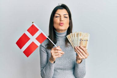 Genç İspanyol kadın elinde Danimarka bayrağı ve Krone banknotları tutarken kameraya bakıp öpüşürken çok güzel ve seksi. aşk ifadesi. 