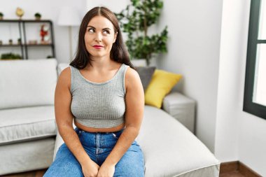 Genç esmer kadın evdeki kanepede oturuyor gülümsüyor yan tarafa bakıyor ve düşünüyor.. 