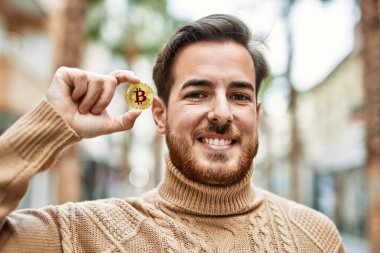 Genç beyaz adam gülerek şehirde bitcoin tutuyor..
