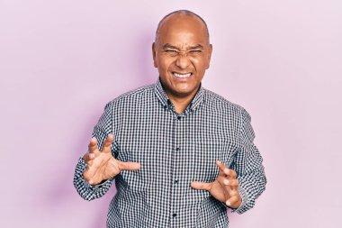 Orta yaşlı, sıradan kıyafetler giyen, tiksindirici ifadeler takınan, tiksindirici, tiksindirici yüz ifadeleri olan Latin bir adam. Eller havada. 