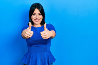 Latin kökenli genç bir kadın, günlük giysiler giyip, olumlu jestler yapıyor, gülümsüyor ve başarı için seviniyor. kazanan jest. 