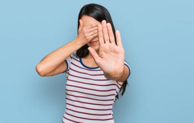 Sıradan çizgili tişört giyen genç İspanyol kız elleriyle gözlerini kapatıyor ve üzgün ve korku ifadeleriyle dur hareketi yapıyor. utangaç ve olumsuz kavram. 