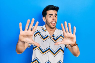 Günlük giysiler giyen genç İspanyol adam korku ifadesinden korkuyor ve dehşete düşüyor. El hareketlerini durdur, şok içinde bağır. panik konsepti. 