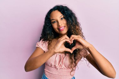 Gündelik kıyafetler giyen, aşık gülümseyen, elleriyle kalp sembolü yapan genç Latin bir kadın. romantik kavram. 